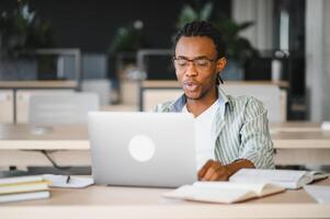 Focused university student studying with laptop and books in library photo