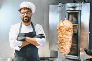 Chef smiling with crossed arms in front of shawarma machine photo
