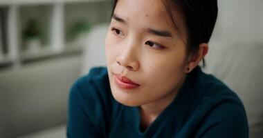 Handheld high angle view shot, A stressed woman is sitting on a sofa with a thoughtful or worried expression on her face in a quiet room at home. Mental health, anxiety, depression video