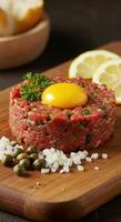 Beef tartare with egg yolk, capers, and lemon slices presented on a wooden board. photo