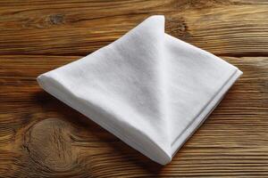 Crisp white linen napkin, neatly folded, rests on a rustic wooden table, showcasing simplicity and photo
