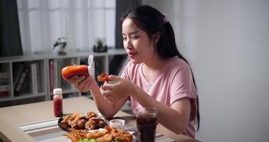 Handheld shot, Asian woman enjoying lunch of fried food and soda on wooden table in living room at home. Lifestyle concept. Enjoying delicious fried food. video