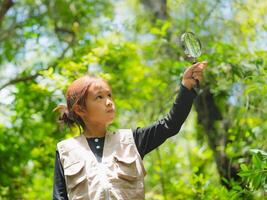 A happy little girl is exploring in the forest and looking for insects with a magnifying glass. Adventure tourism and learning. photo
