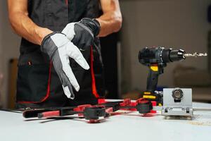 Man puts on protective gloves, prepares to start work in carpentry workshop. Close-up of worker near workbench with woodworking tools and electric drill photo