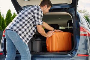 Man loading suitcase into car trunk before journey. Packing luggage for travel photo