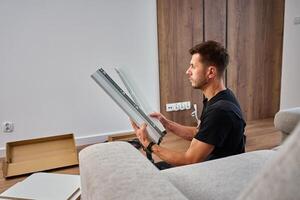 Man assembles furniture, examining white panel and surrounded by tools photo