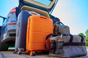 Suitcases and bags in front of open car trunk, standing on pavement near suburban house. Luggage ready for loading in vehicle before travel or moving. Concept of relocation or road trip photo