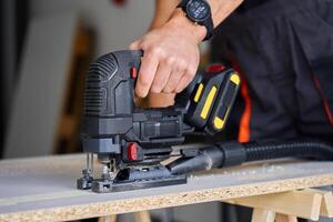 Close up of electrical handheld jigsaw cutting wooden board in workshop photo
