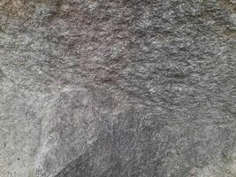 Close-up of a natural rock surface with a rough, uneven texture, visible cracks, and earthy tones, showing signs of weathering and mineral deposits photo