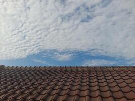 A tiled rooftop under a sky filled with scattered clouds and patches of blue. The scene captures a peaceful, sunny day with a blend of architectural and natural elements. photo