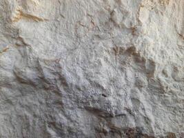 Rough and uneven stone surface with a mix of light and dark earthy tones, showing natural erosion, layers, and mineral textures. photo