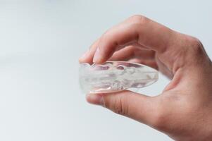 Man holding orthodontic silicone mouth guard for teeth straightening or whitening. Side view, close-up, on white background photo