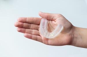 A mouth guard for bite alignment or teeth whitening lies on a person's palm. Top view, close-up, on a white background photo