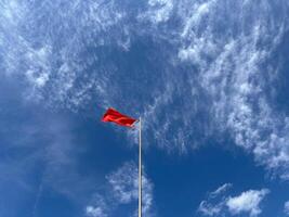 Red flag raised in the sky. Red flag fluttering in the wind. Symbol of prohibition and danger. photo