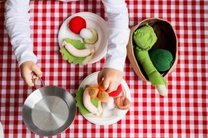 Child playing with colorful felt vegetables on red checkered tablecloth photo