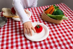 Child playing with toy vegetables on checkered tablecloth photo