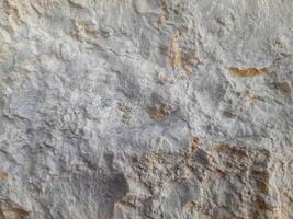 Rough stone surface with mixed beige and gray tones, showing natural erosion, uneven texture, and layered mineral patterns photo