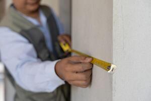 inspector or engineer inspecting construction and quality assurance check dimension of house by using a tape measurement. Engineers or architects or contactor work to build the house before sell. photo