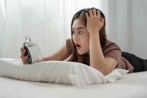 Shocked Asia young woman look clock alarm, lady is late appointment or work or class study, overslept, difficulty get up in mornings, time worried, not on time, sleepy, over due, Hurry up time photo