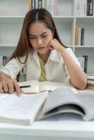 Asian student woman have anxiety because of exams, female prepare for test and learning lessons in the library. stress, despair, haste, misunderstanding reading,, expectation, knowledge photo