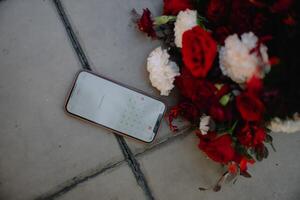 a smartphone is lying on the ground next to a bouquet of red flowers photo