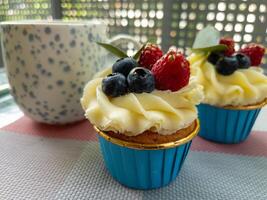 Cupcake with Berries and Coffee Mug on Outdoor Table. Delicious cupcake with cream frosting, blueberries, raspberries photo