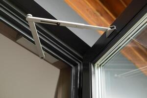 Close-up of a modern window hinge mechanism in an open aluminum-framed window, showing construction detail and engineering design photo