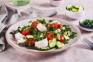 Homemade salad with cucumber, tomatoes, chicken and herbs on a plate on the table photo