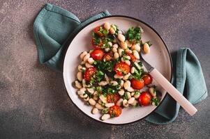 Close up of appetizing salad of white beans, cherry tomatoes and parsley on a plate top view photo