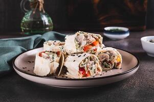 Chicken meat, pepper and cucumber in sauce wrapped in tortilla rolls on a plate on a table photo