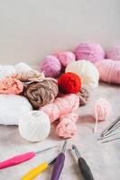 Lots of colorful skeins of yarn, crochet hooks and knitting needles on a table vertical view photo