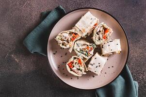 Close up of chicken meat, pepper and cucumber in sauce wrapped in tortilla rolls on a plate top view photo