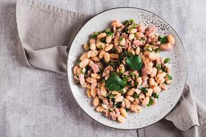 Close up of appetizing salad with tuna, white beans and greens on a plate on the table top view photo