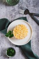 Classic mimosa salad with canned fish and vegetables on a plate on the table top and vertical view photo