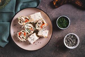 Chicken meat, pepper and cucumber in sauce wrapped in tortilla rolls on a plate top view photo