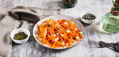 Spicy carrot, ricotta and pumpkin seed salad on a plate on a table web banner photo