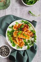 Crispy fried halloumi cheese and arugula leaves on a plate on a table top and vertical view photo