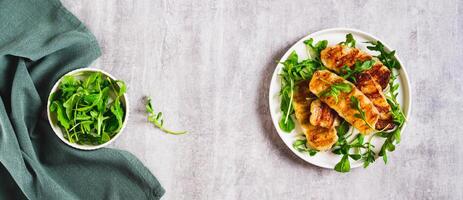 Crispy fried halloumi cheese and arugula leaves on a plate on a table top view web banner photo