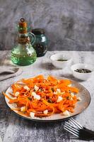 Spicy carrot, ricotta and pumpkin seed salad on a plate on a table vertical view photo