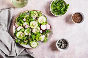 Vegetarian salad with cucumber, radish and arugula on a plate on the table top view photo