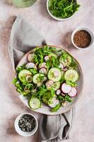 Cucumber, radish and greens salad mix on a plate on the table top and vertical view photo