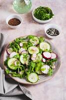 Cucumber, radish and greens salad mix on a plate on the table vertical view photo