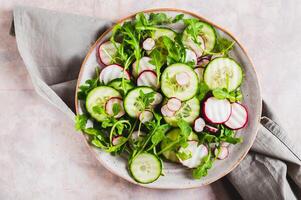 Close up of vegetarian salad with cucumber, radish and arugula on a plate on the table top view photo