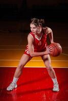 Focused female basketball player in red uniform in dribble stance on indoor court, showing determination, control, and readiness for game action. photo