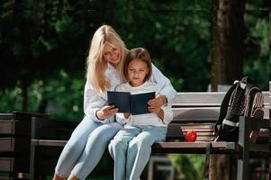 Information in notepad, ,,,,reading it. Little schoolgirl with her mother are sitting on the bench outdoors photo