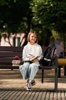 Writing ideas into notepad. Schoolgirl,,, is sitting on the bench with a bunch of books outdoors photo