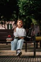 Writing ideas into notepad. Schoolgirl is sitting on the bench with a bunch of books ,outdoors photo