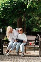 Information, in notepad, reading it. Little schoolgirl with her mother are sitting on the bench outdoors photo