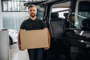 Big order, holding ,,the box. Delivery man, or ,loader is near the car with photo
