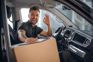 Showing hand gesture, everything ,,is, fine, will be done. The delivery man or a loader is in the car with box photo